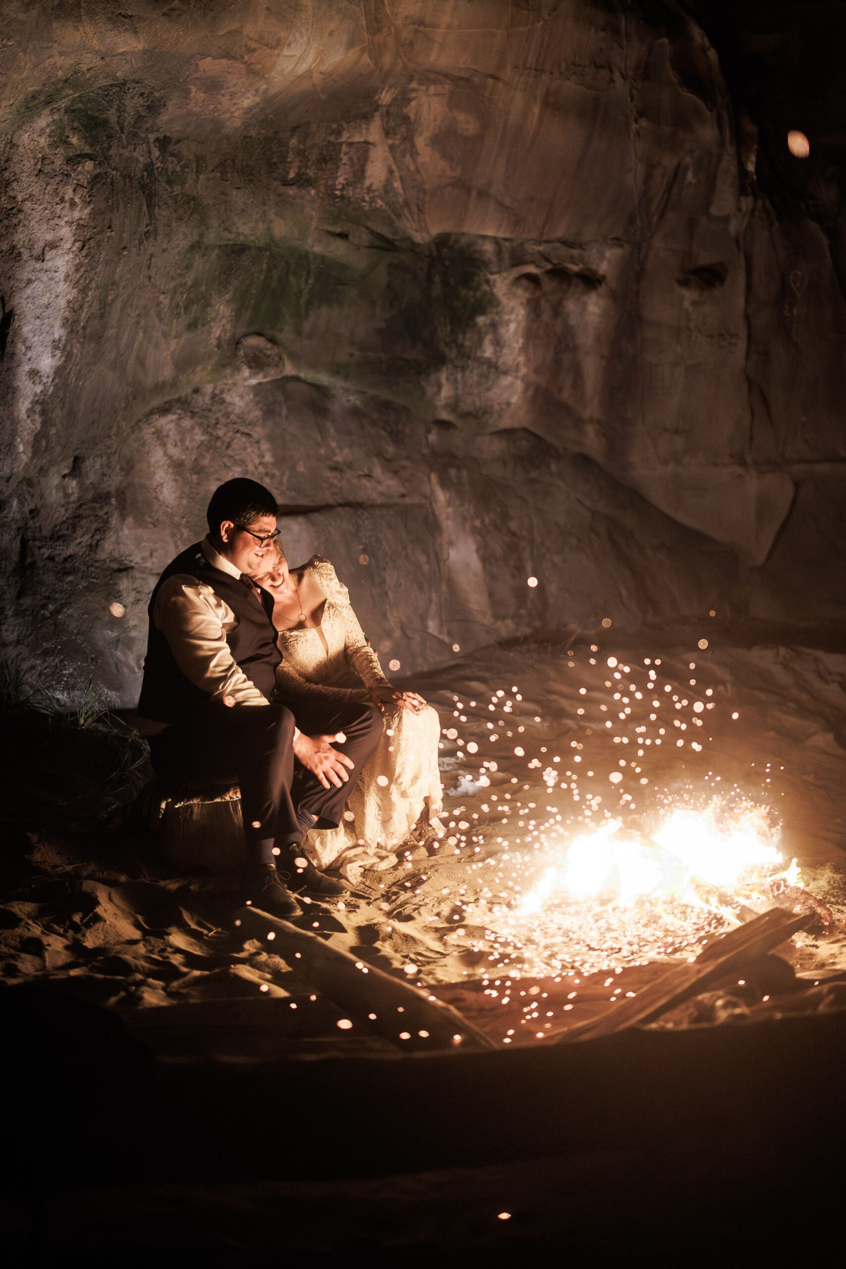 bridal couple sitting by the fire on the beach