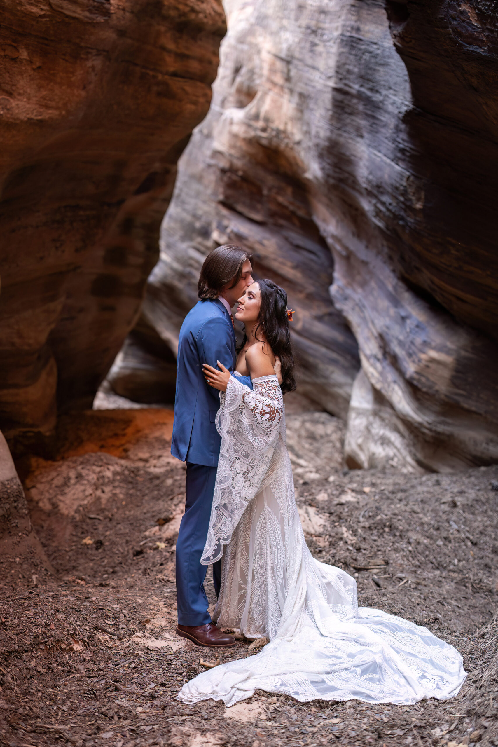 groom kissing a bride on the forehead in a slot canyon