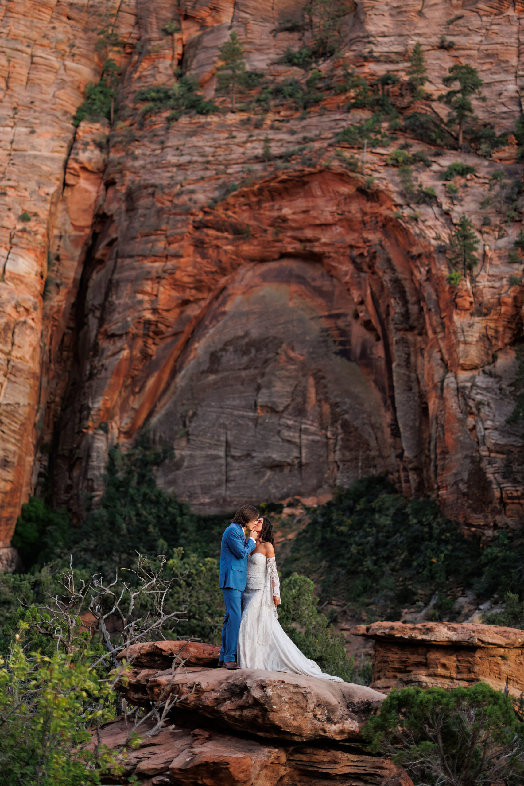 a couple in zion kissing with a big red rock wall behind them 