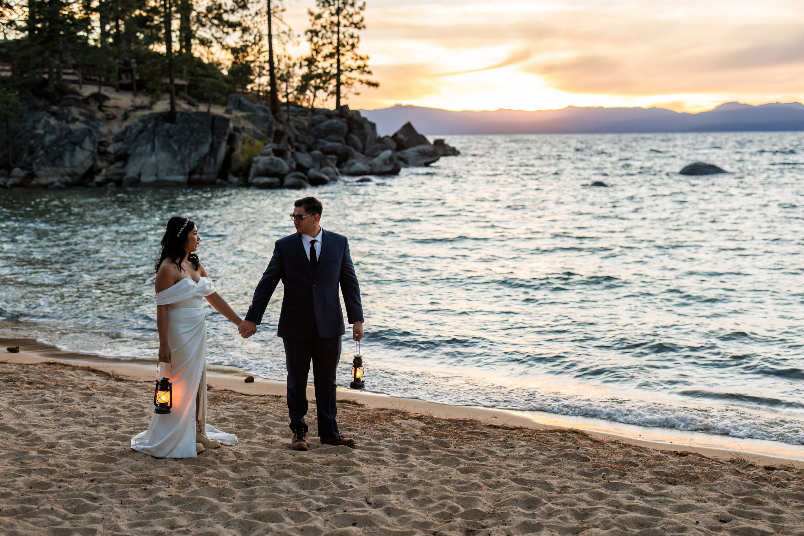 a couple standing on the beach holding lanterns as the sun sets