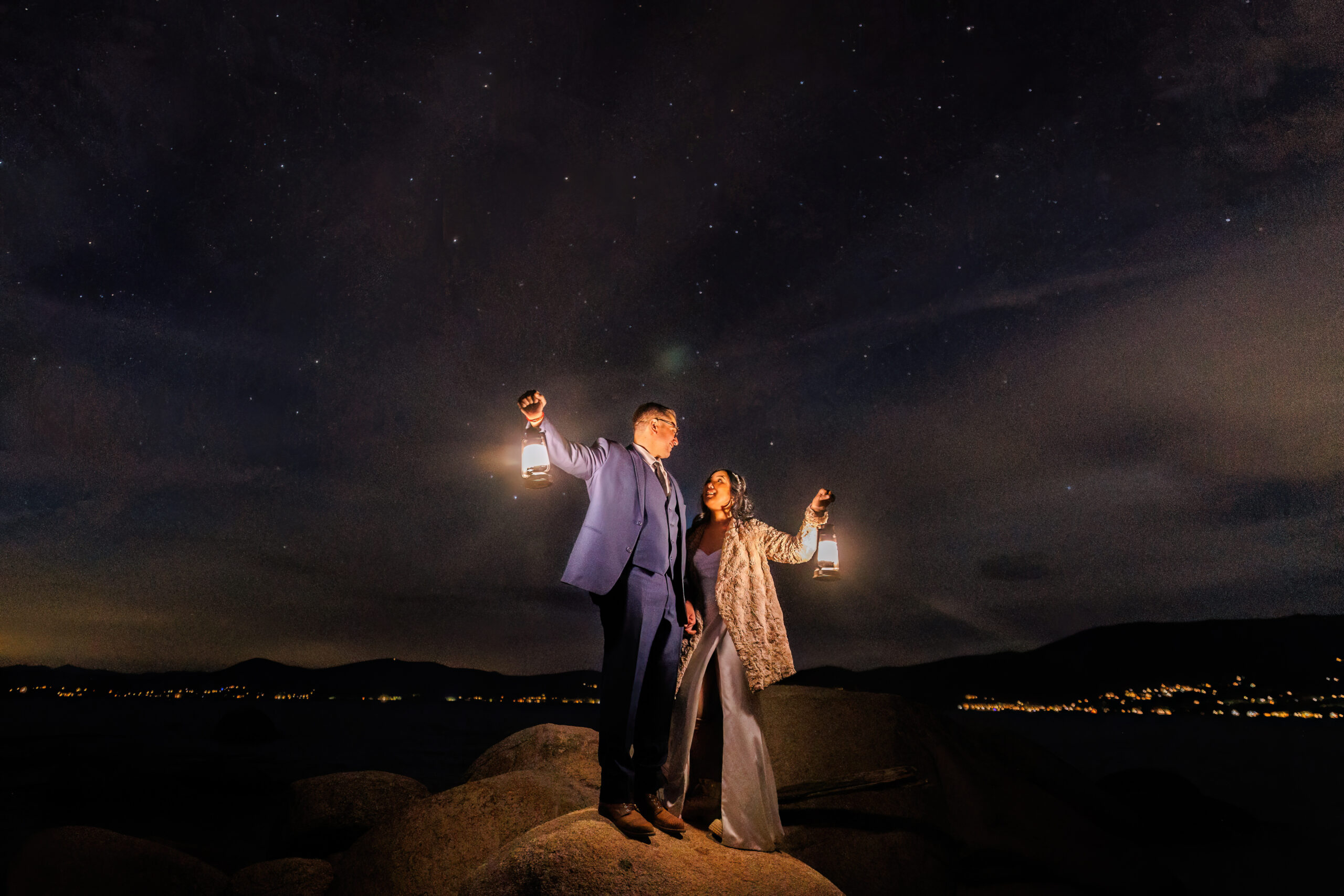 a night elopement photo as the couple standing on a rock while holding lanterns 