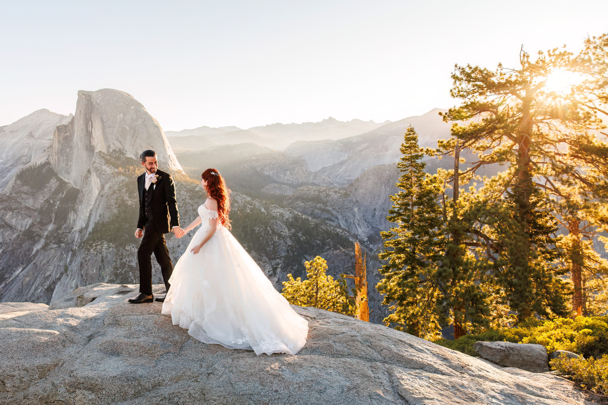 a man and woman walking on the rocks as the sun shines through the trees during their mountain elopement