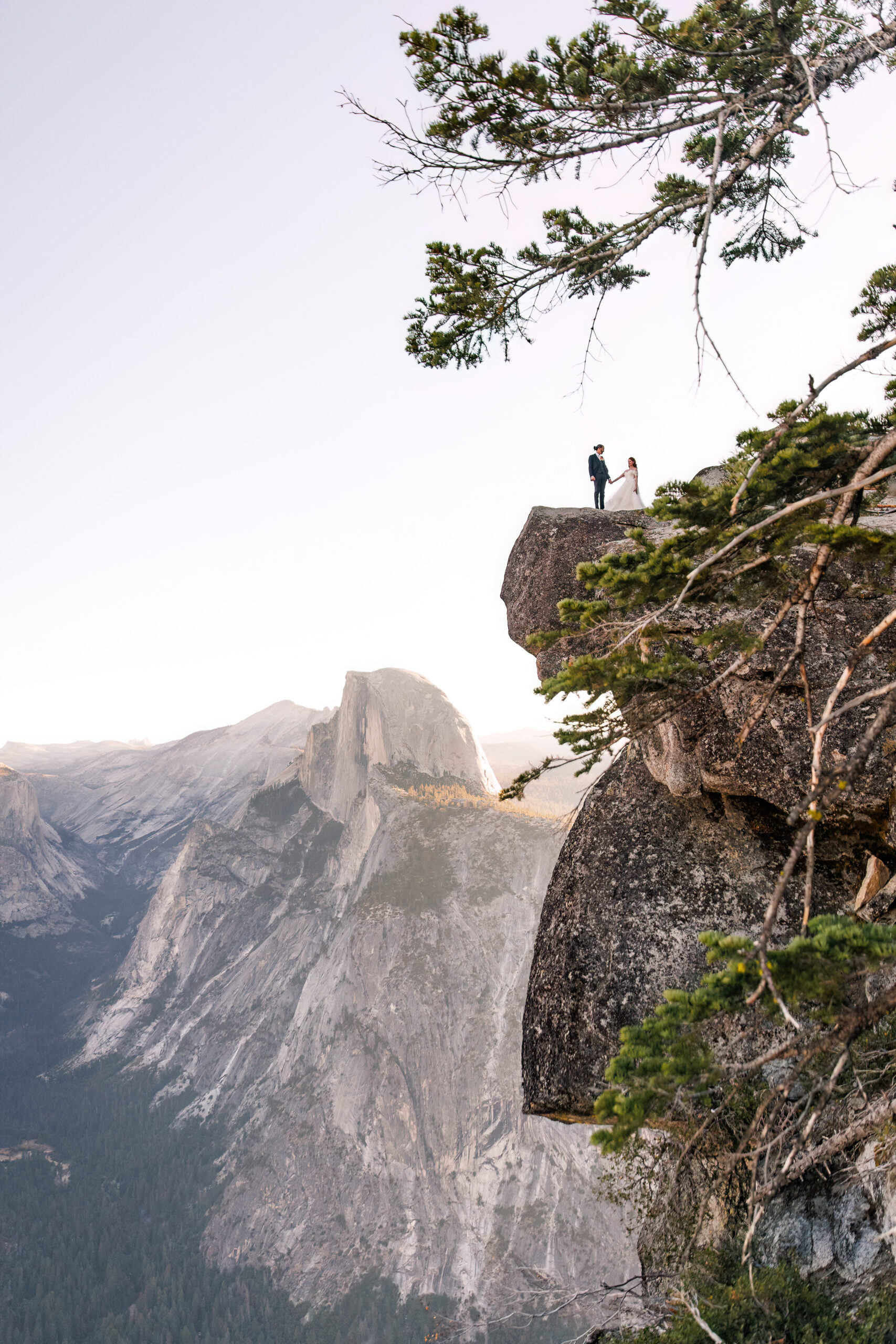 a couple standing on a rock ledge from far away during their mountain elopement 