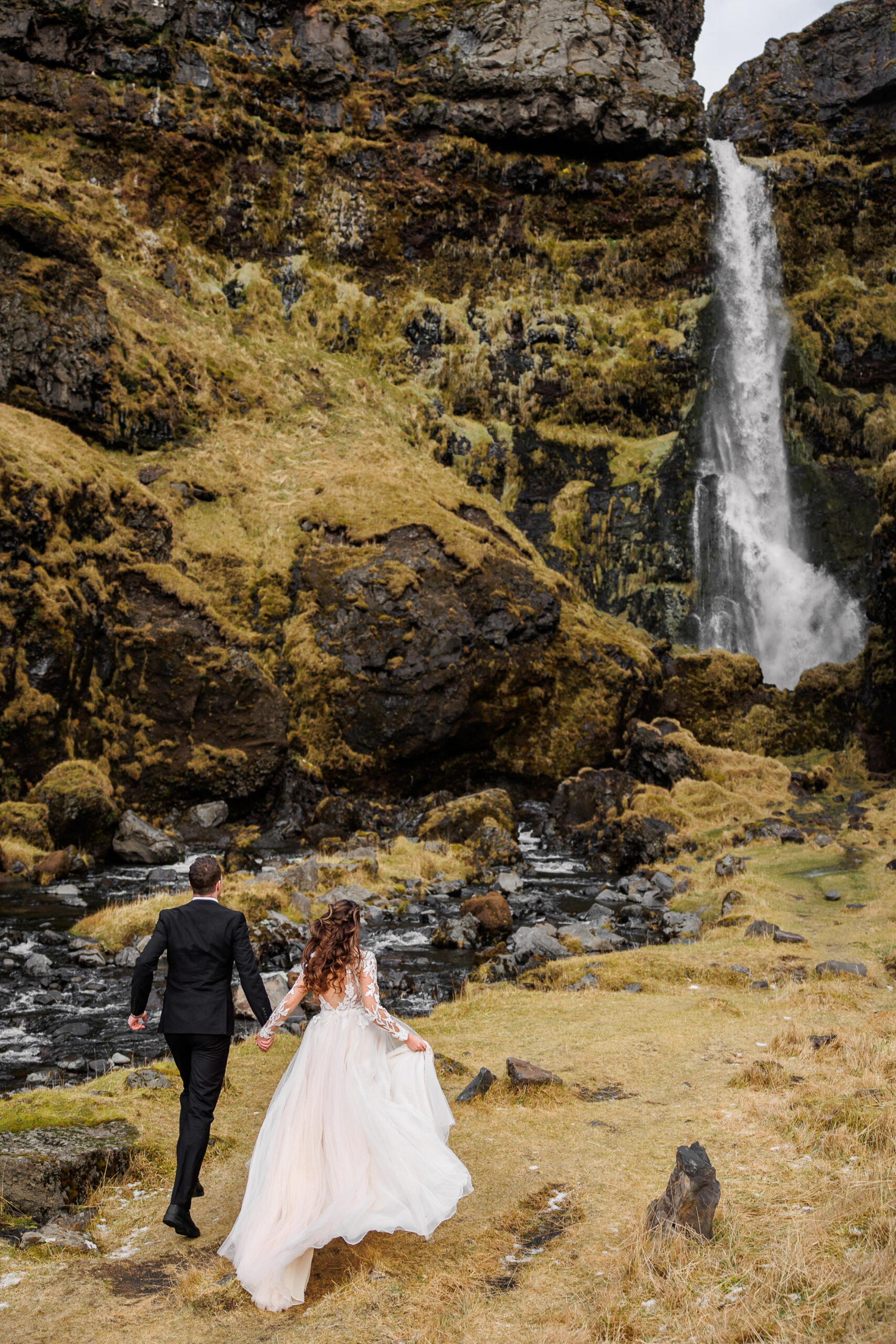 a mountain elopement in Iceland as a couple runs toward a waterfall