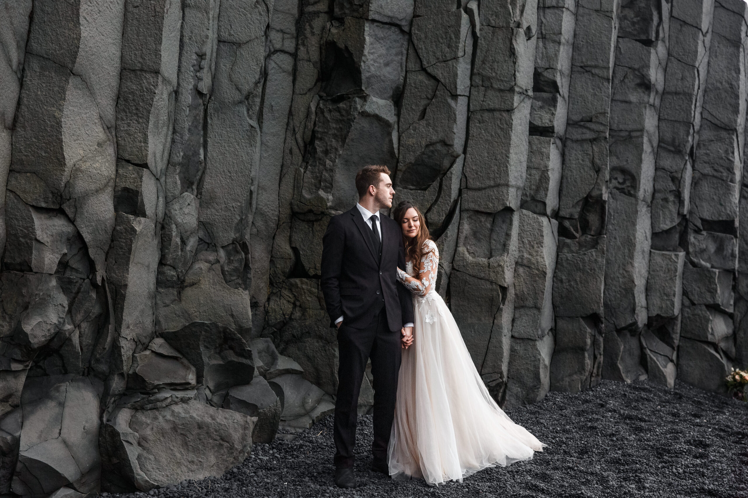 bride and groom standing in front of a wall of black rock 